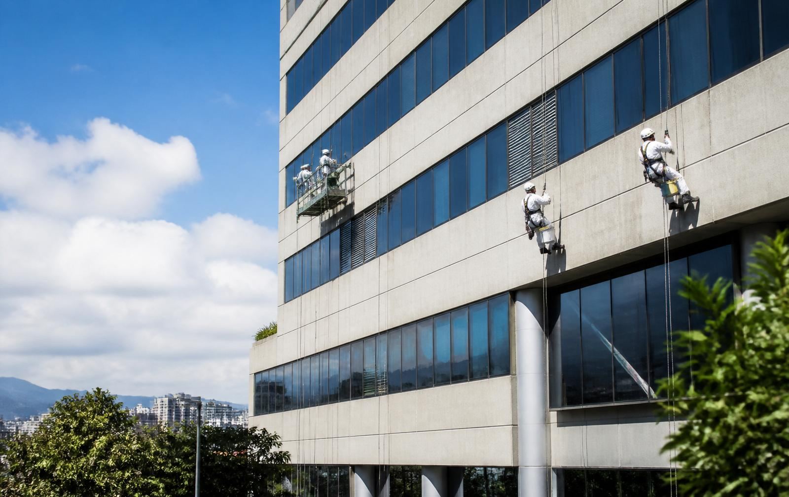Trabajadores certificados en plataformas suspendidas realizando limpieza de fachada de edificio en Bogotá